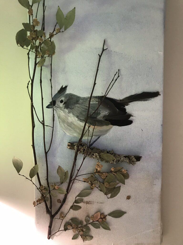 A painting of a bird accented with a real tree branch.